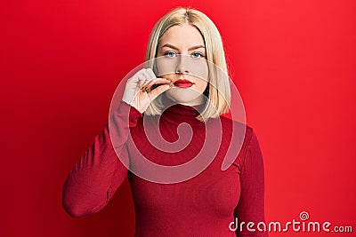 Young blonde woman wearing casual clothes mouth and lips shut as zip with fingers Stock Photo