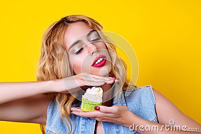 Young blondy model is enjoyment with delicious cupcake over yellow background. Stock Photo