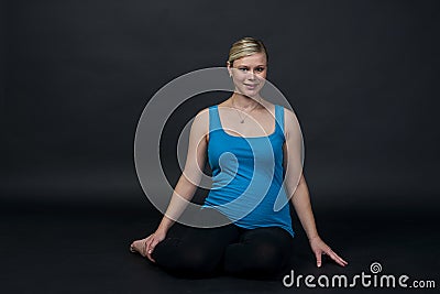 Young blondy pregnant woman in blue tank top does exercises, black background. Stock Photo