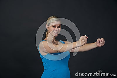 Young blondy pregnant woman in blue tank top does exercises, black background. Stock Photo
