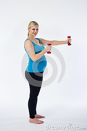 Young blondy pregnant woman in blue tank top does exercises with small red fitness dumbbells, white background. Stock Photo