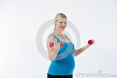 Young blondy pregnant woman in blue tank top does exercises with small red fitness dumbbells, white background. Stock Photo