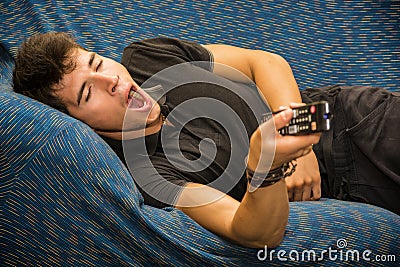 Young bored man sitting on sofa watching Stock Photo