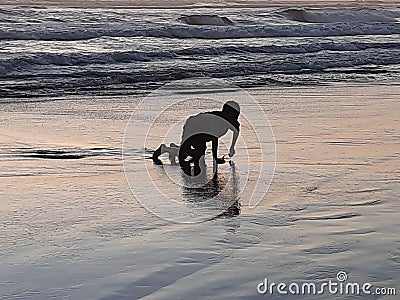 A young boy on all fours playing and enjoying alone the wet and reflecting sand at sunset time at Parangtritis Beach, Java, Indone Stock Photo