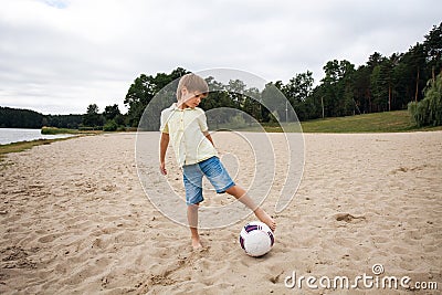 A young boy on the beach runs towards a soccer ball and wants to score a goal Stock Photo