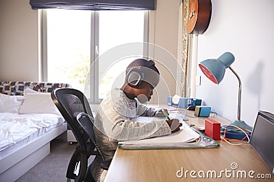 Young Boy In Bedroom Wearing Headphones And Doing Homework Stock Photo