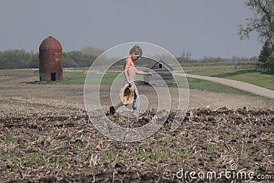 Young boy crosses field carrying straw hat Stock Photo