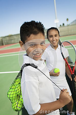 Young boy and girl with tennis equipment on tennis court focus on boy portrait Stock Photo