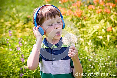 Young boy in headphones listening to modern music in nature. Child likes the song and look to giant dandelion. Kid music relax Stock Photo
