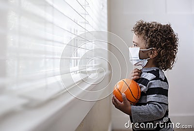 Young boy looking out the window wearing a protective facemark while seeking protection from COVID-19, or the novel coronavirus Stock Photo
