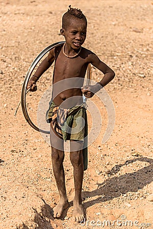 A young boy playing with a bicycle or cart wheel, Epupa falls, Namibia Editorial Stock Photo