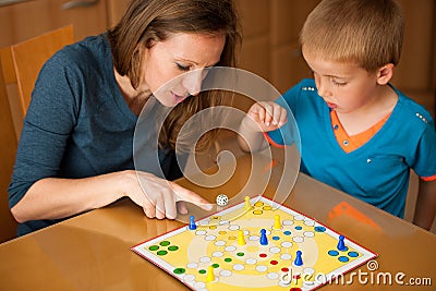 young boy plays ludo game with his mother on a table in livingroom Stock Photo