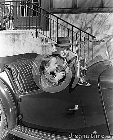 Young boy sitting in the driver's seat of car with his father Stock Photo