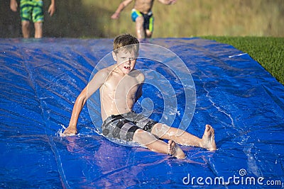 Young boy sliding down a slip and slide outdoors Stock Photo