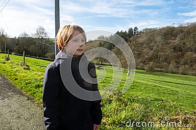 Young boy stands on road in countryside. Boy of eight ten years of old age with long red hair in warm jacket. Walking, active Stock Photo