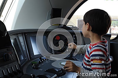 A young boy steering a locomotive and train in a driving compartment or cabin with handles and meters as a train driver Stock Photo