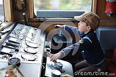 A young boy steering a locomotive and train in a driving compartment or cabin with handles and meters as a train driver Stock Photo