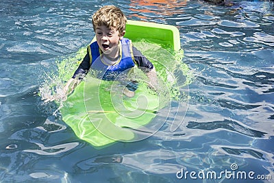 Young boy in swimming pool with green plastic boat Stock Photo