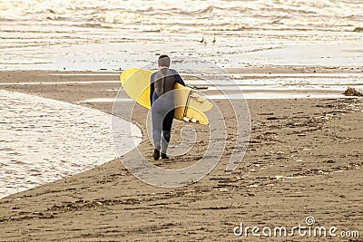 Young boy walking toward ocean with wetsuit and yellow surfboard - almost monochromatic in browns and ochers Editorial Stock Photo