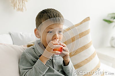 Young boy 6-7 years old siitng on bed, eating apple. Home lifestyle concept Stock Photo