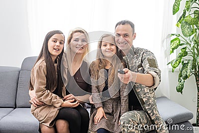 Young brave soldier spending quality time with his family. They are watching television. Man having remote control in Stock Photo