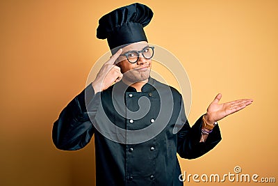 Young brazilian chef man wearing cooker uniform and hat over isolated yellow background confused and annoyed with open palm Stock Photo