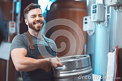 A young brewer in an apron holds a barrel with beer in the hands Stock Photo