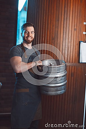 A young brewer in an apron holds a barrel with beer in the hands Stock Photo