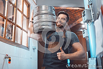 A young brewer in an apron holds a barrel with beer in the hands Stock Photo