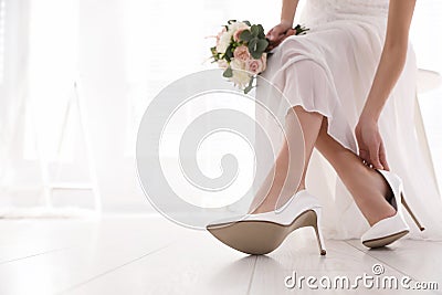 Young bride putting on beautiful wedding shoes indoors closeup. Space for text Stock Photo