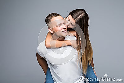Love forever. Young brunete handsome boyfriend is piggy backing his cute lover, wearing casual clothes, on gray background Stock Photo
