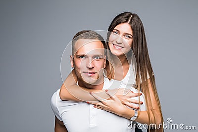 Love forever. Young brunete handsome boyfriend is piggy backing his cute lover, wearing casual clothes, on gray background Stock Photo