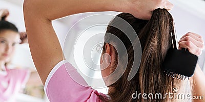 Young brunette brushes hair in ponytail at mirror back view Stock Photo