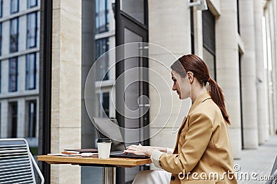 Young brunette businesswoman in beige formalwear using laptop in street cafe Stock Photo