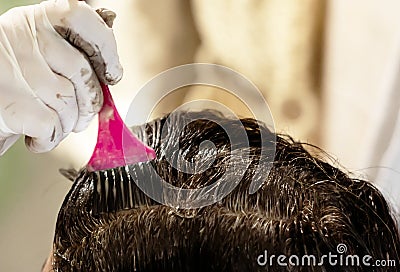 A young brunette caucasian woman dying her hair with a pink brush using white gloves at her home Stock Photo