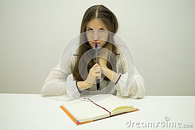 Young brunette girl with flowing hair sits at a table with a diary on the table Stock Photo