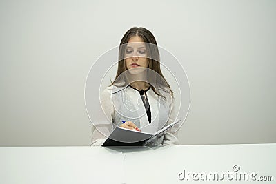 Young brunette girl with her hair straight sits at the table with a notebook in her hands Stock Photo