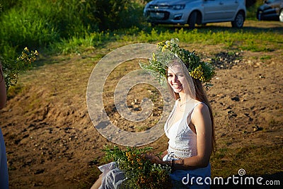 Young brunette girl in a white dress, sundress and a wreath of flowers in summer on the coast of river or lake in the Stock Photo