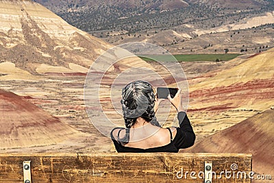 A young brunette with gray strands takes photographs with her smartphone sitting on a bench in Painted Hills Overlook Stock Photo