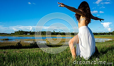 Young brunette spanish woman doing warrior 2 yoga pose in a field next to a lake with long curly hair Stock Photo