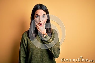 Young brunette woman with blue eyes wearing green casual sweater over yellow background Looking fascinated with disbelief, Stock Photo