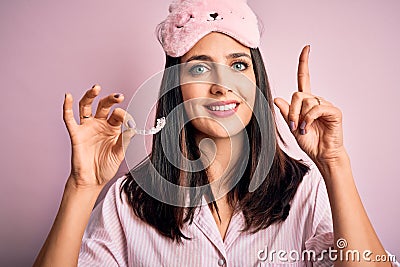 Young brunette woman with blue eyes wearing pajama holding dentist clear aligner surprised with an idea or question pointing Stock Photo