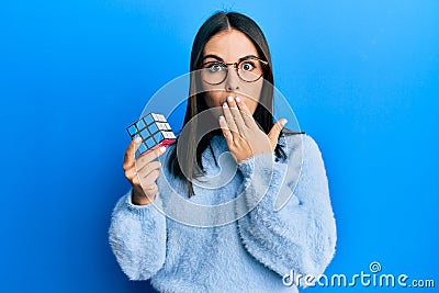 Young brunette woman playing colorful puzzle cube intelligence game covering mouth with hand, shocked and afraid for mistake Editorial Stock Photo