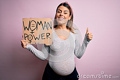Young brunette woman pregnant expecting baby holding banner asking for women power happy with big smile doing ok sign, thumb up Stock Photo