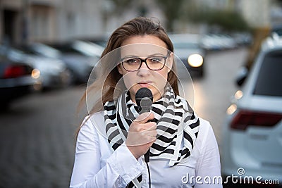 Young woman standing on street with microphone and talking Stock Photo