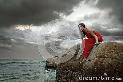 Young brunette woman in summer red dress sits on stone Stock Photo