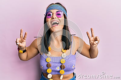 Young brunette woman wearing bohemian and hippie style doing peace symbol smiling and laughing hard out loud because funny crazy Stock Photo