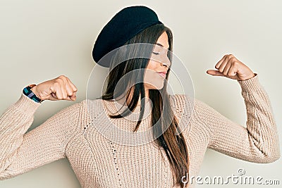 Young brunette woman wearing french look with beret showing arms muscles smiling proud Stock Photo