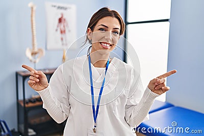 Young brunette woman working at pain recovery clinic smiling confident pointing with fingers to different directions Stock Photo