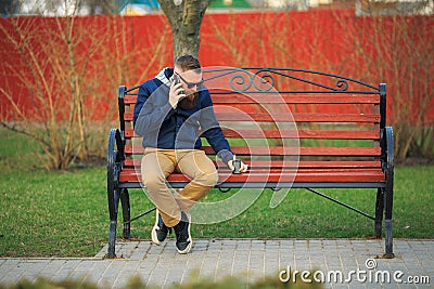 Young brutal man with large beard and fashionable haircut in sunglasses talking on mobile phone. Stock Photo